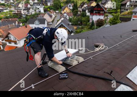 Forbach, Allemagne. 10 juillet 2024. Un technicien installe une antenne satellite Starlink sur un toit. Dans le cadre d’un projet pilote de couverture de téléphonie mobile en milieu rural, Vodafone coopère avec la société américaine Starlink, dont les satellites peuvent actuellement fournir un accès Internet rapide dans toute l’Europe, l’Amérique du Nord, l’Amérique du Sud et l’Australie. À cet effet, l'opérateur mobile a installé un mât de transmission à Forbach, qui établit le contact avec les serveurs de Vodafone à Francfort via Starlink. Crédit : Philipp von Ditfurth/dpa/Alamy Live News Banque D'Images