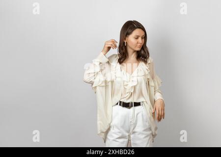 Une femme élégante dans une blouse blanche à volants et un pantalon blanc se tient gracieusement. Parfait pour la mode et les thèmes de style de vie. Banque D'Images