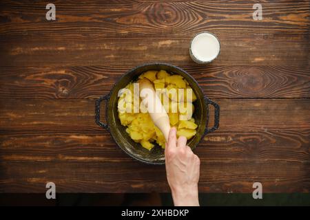 La main de la femme tient le presse-purée en bois et fait de la purée de pommes de terre, vue de dessus Banque D'Images