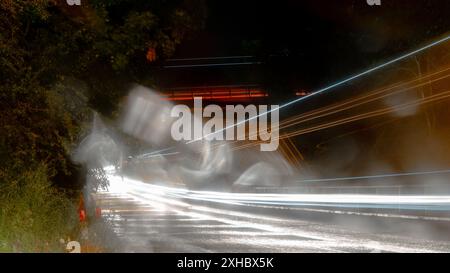 La circulation traîne par une nuit humide et orageuse. Avec bokeh et gouttes de pluie. Banque D'Images