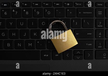 Un cadenas doré repose sur un clavier noir d'ordinateur portable, le moraillon du cadenas reposant sur la touche entrée. Banque D'Images