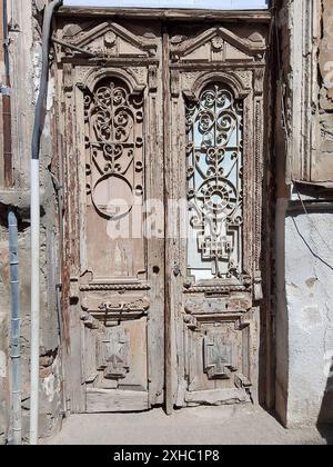 Cette image capture le charme rustique d'une paire de portes en bois vieilli, chacune ornée de ferronneries et de motifs complexes. Les portes servent de test Banque D'Images