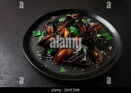 Spaghetti au calmar noir, pâtes noires, avec des moules bouillies, sur une assiette noire, avec du persil et du parmesan, gros plan, focus sélectif, pas de gens Banque D'Images