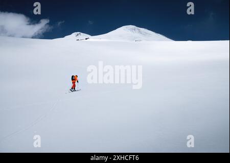 Un jeune skieur sportif en combinaison orange grimpe à ski sur une pente enneigée jusqu'au mont Elbrus. Copier l'espace. Alpinisme hivernal Banque D'Images