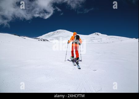 Un jeune skieur sportif en combinaison orange grimpe à ski sur une pente enneigée jusqu'au mont Elbrus. Copier l'espace. Alpinisme hivernal Banque D'Images