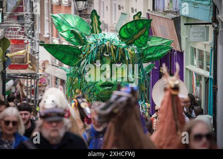 Folkestone, Kent, Royaume-Uni. 13 juillet 2024. Défilé annuel du Charivari Day. Folklore britannique et traditions rituelles sont le thème de la saisissante parade du carnaval de cette année. Des sculptures massives de tête ornent les épaules des jeunes locaux avec des enfants de l'école primaire à travers le district habillant aux couleurs du thème de l'année. Marchant du stade, en passant par la ville jusqu’au kiosque à musique Leas, le Charivari Day reste la plus grande tradition coutumière de Folkestone depuis 1997 et attire des centaines de spectateurs dans la ville portuaire en bord de mer. Crédit : Guy Corbishley/Alamy Live News Banque D'Images