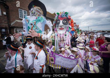 Folkestone, Kent, Royaume-Uni. 13 juillet 2024. Défilé annuel du Charivari Day. Folklore britannique et traditions rituelles sont le thème de la saisissante parade du carnaval de cette année. Des sculptures massives de tête ornent les épaules des jeunes locaux avec des enfants de l'école primaire à travers le district habillant aux couleurs du thème de l'année. Marchant du stade, en passant par la ville jusqu’au kiosque à musique Leas, le Charivari Day reste la plus grande tradition coutumière de Folkestone depuis 1997 et attire des centaines de spectateurs dans la ville portuaire en bord de mer. Crédit : Guy Corbishley/Alamy Live News Banque D'Images