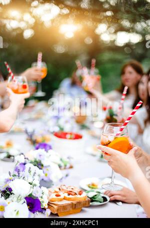 Des personnes méconnaissables avec des verres d'alcool de fruits proposant des toasts tout en étant assis à table pendant le banquet dans le jardin le jour d'été Banque D'Images