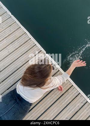 Vue de dessus de jeune femme méconnaissable allongé sur le quai et barbotant eau propre du lac le jour d'été Banque D'Images