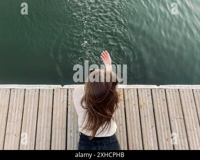 Jeune femme brune allongé sur le quai et barbotant de l'eau propre du lac le jour de l'été Banque D'Images