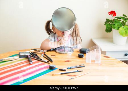 Adorable petit enfant avec le visage sale jouant avec des cosmétiques et faisant le maquillage tout en regardant dans le miroir Banque D'Images