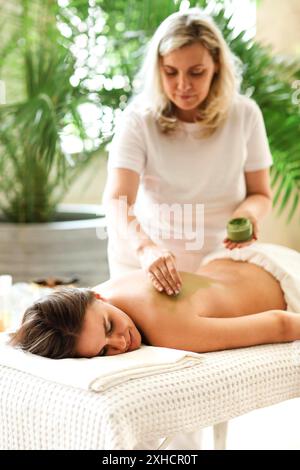 Belle femme détendue ayant le masque d'argile s'appliquant à l'arrière dans le salon de spa Banque D'Images