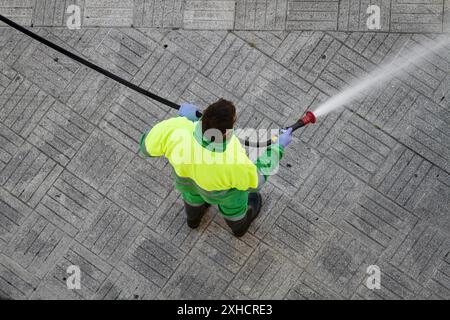 Un travailleur tenant un tuyau pour nettoyer le trottoir avec de l'eau. Entretien urbain ou concept de nettoyage Banque D'Images