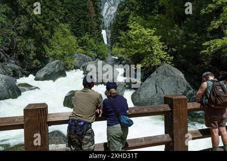 Les randonneurs debout sur le John Muir Trail Bridge regardent le fleuve Merced qui coule rapidement dans le parc national de Yosemite, Californie, États-Unis au printemps 2005 Banque D'Images