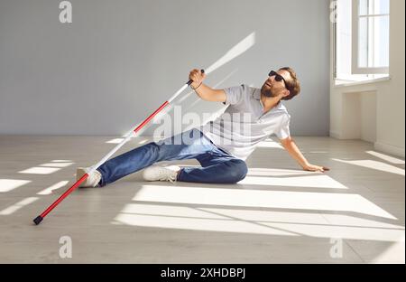 Homme malvoyant et sourd tombe sur le sol en marchant avec la canne à la maison Banque D'Images