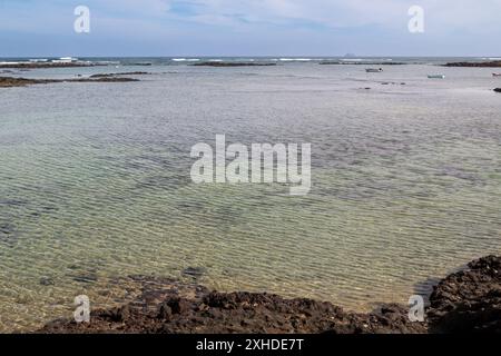 Plage avec sable blanc et une eau peu profonde. Petites roches volcaniques noires. Ciel bleu avec des nuages légers en hiver. Caleton Blanco, Lanzarote, Îles Canaries Banque D'Images