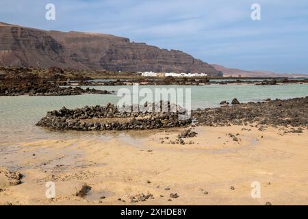 Plage avec sable blanc et une eau peu profonde. Petites roches volcaniques noires. Ciel bleu avec des nuages légers en hiver. Caleton Blanco, Lanzarote, Îles Canaries Banque D'Images