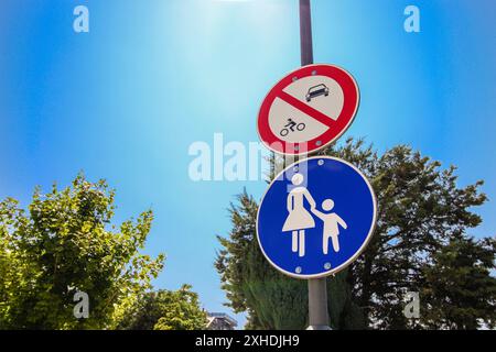 Un panneau bleu pour piétons et un panneau rouge d'interdiction de véhicule ou de bicyclette, montés sur un poteau de lampadaire contre un ciel bleu vif d'été. Banque D'Images