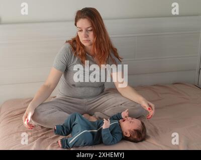Une femme caucasienne est assise sur un lit à côté d'un bébé qui pleure. Dépression du post-partum. Banque D'Images