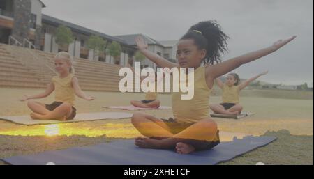 Image de paysage de coucher de soleil sur des écolières diversifiées heureuses s'étirant dans un cours de yoga en plein air Banque D'Images
