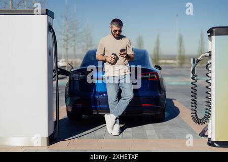 Homme utilisant smartphone tout en chargeant la voiture électrique Banque D'Images