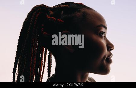 Jeune femme africaine aux cheveux tressés coiffés en queue de cheval. Elle est vue dans un gros plan de tête, regardant au loin avec une vue de côté. Le fond blanc emp Banque D'Images