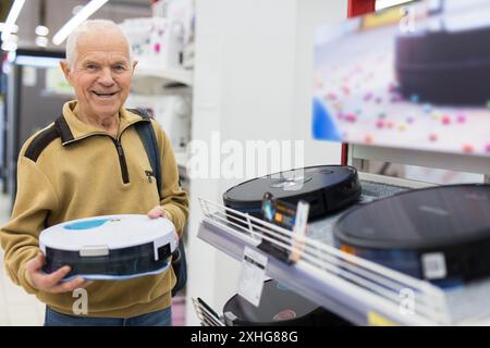 Senor homme retraité achetant aspirateur robotique dans la salle d'exposition du magasin d'appareils électriques Banque D'Images