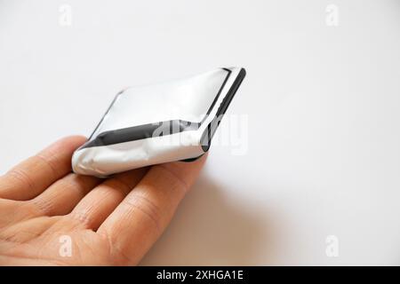 Une batterie de téléphone gonflée par la surchauffe dans les mains d'une fille repose sur un fond blanc, la batterie de téléphone est gonflée Banque D'Images