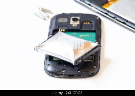 Une batterie de téléphone gonflée à cause de la surchauffe et un téléphone démonté reposent sur un fond blanc, la batterie du téléphone est gonflée, réparation du téléphone Banque D'Images