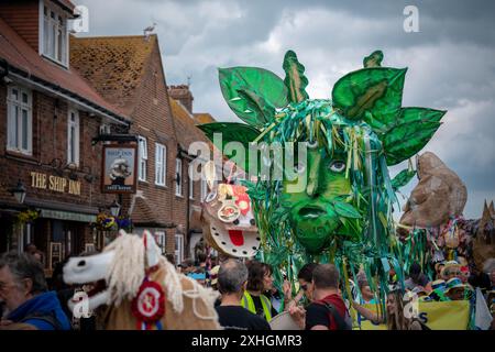 Folkestone, Kent, Royaume-Uni. 13 juillet 2024. Défilé annuel du Charivari Day. Folklore britannique et traditions rituelles sont le thème de la saisissante parade du carnaval de cette année. Des sculptures massives de tête ornent les épaules des jeunes locaux avec des enfants de l'école primaire à travers le district habillant aux couleurs du thème de l'année. Marchant du stade, en passant par la ville jusqu’au kiosque à musique Leas, le Charivari Day reste la plus grande tradition coutumière de Folkestone depuis 1997 et attire des centaines de spectateurs dans la ville portuaire en bord de mer. Crédit : Guy Corbishley/Alamy Live News Banque D'Images