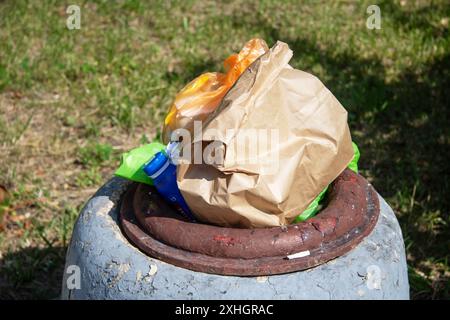 Un sac en papier brun se trouve au sommet d'une poubelle à côté d'une bouche d'incendie et de l'herbe Banque D'Images