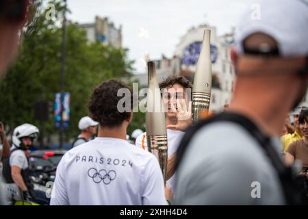 14 juillet 2024, Paris, France. Les porteurs de flammes se saluent alors que la flamme olympique traverse la place de la Bastille, traversant Paris. Crédit : Jay Kogler/Alamy Live News Banque D'Images