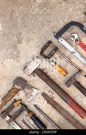 Vieux outils de construction disposés sur un fond de béton, vue de dessus. Marteau, pince de construction, lime plate, marteau de forge, scie à main et pince. Collectiti Banque D'Images