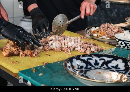 Les chefs masculins coupent de la viande de bœuf bouillie avec des couteaux sur une planche à découper dans la cuisine d'un restaurant en Ouzbékistan Banque D'Images