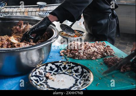 Les chefs masculins coupent la viande de bœuf bouillie avec des couteaux pour cuisiner le pilaf ouzbek oriental dans la cuisine au restaurant à Tachkent en Ouzbékistan Banque D'Images