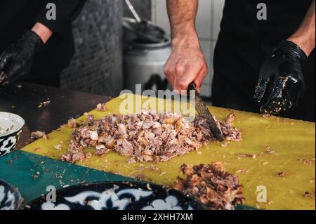 Les chefs masculins coupent de la viande de bœuf bouillie avec des couteaux sur une planche à découper dans la cuisine d'un restaurant à Tachkent en Ouzbékistan Banque D'Images