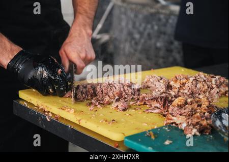 Les mains du chef masculin coupent la viande bouillie avec un couteau pour cuisiner le pilaf ouzbek traditionnel dans le restaurant Central Asian Pilaf Center Besh Qozon à Tachkent en Ouzbékistan Banque D'Images