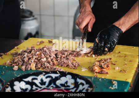 Chef mâle couper la viande d'agneau bouillie avec un couteau pour cuisiner le pilaf oriental traditionnel ouzbek dans un restaurant à Tachkent en Ouzbékistan de près Banque D'Images