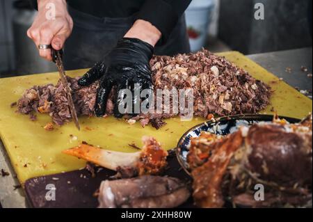 Homme chef des mains coupent la viande d'agneau bouillie avec un couteau pour cuisiner le pilaf ouzbek traditionnel asiatique dans un restaurant à Tachkent en Ouzbékistan Banque D'Images