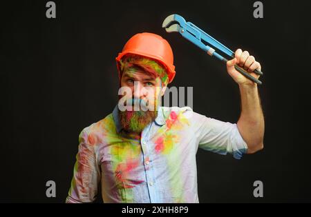 Homme barbu dans un casque de protection avec clé à tube ou clé de plomberie. Service de réparation. Plombier sérieux ou réparateur dans un casque de sécurité avec plomb wrenc Banque D'Images