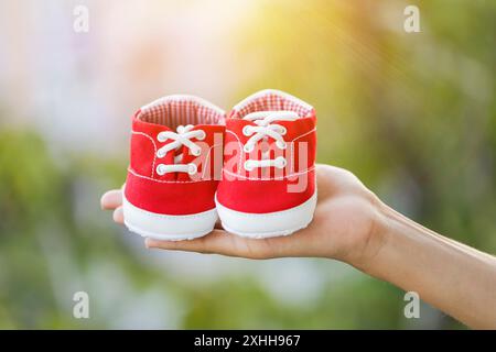 Une main tenant des chaussures de bébé rouges Banque D'Images