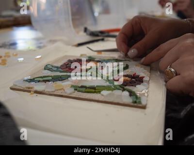 Atelier de mosaïque : un gros plan horizontal sur une table capture les mains d'une femme créant un motif de mosaïque florale. Banque D'Images