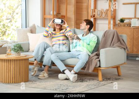 Jeune homme avec téléphone portable et sa petite amie utilisant des lunettes VR à la maison Banque D'Images