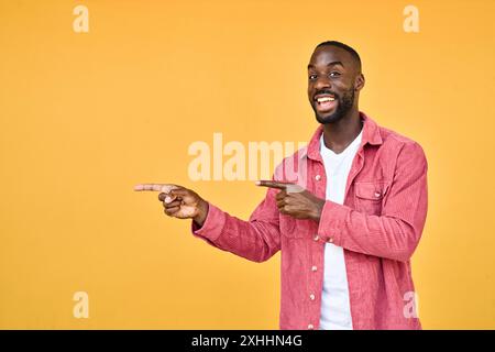 Heureux jeune homme afro-américain debout isolé sur le jaune pointant latéralement. Banque D'Images