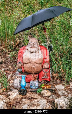 Drôle de skulpture de bouddha en bord de route sous un parapluie à Hua Hin, Thaïlande Banque D'Images