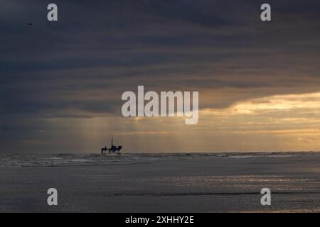 Vue sur une plate-forme de production offshore au lever du soleil, sous des nuages sombres et au loin une clairière et de la pluie Banque D'Images