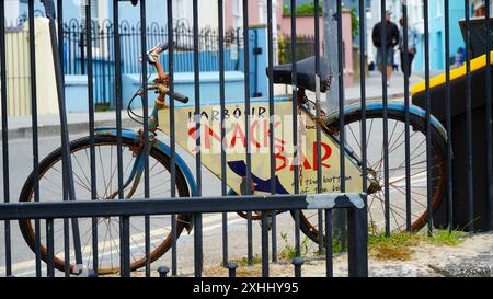 Tenby, Pembrokeshire, pays de Galles - 02 juillet 2024 : une vieille poussette peinte, vélo avec un panneau fixé à elle est utilisé pour diriger les touristes vers un snack-bar. Banque D'Images