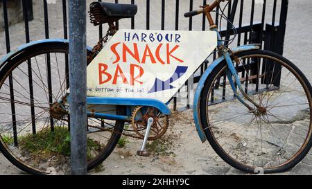 Tenby, Pembrokeshire, pays de Galles - 02 juillet 2024 : une vieille poussette peinte, vélo avec un panneau fixé à elle est utilisé pour diriger les touristes vers un snack-bar. Banque D'Images