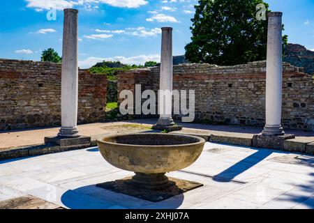 De hautes colonnes blanches se dressent au milieu d'anciennes ruines de briques à Felix Romuliana, en Serbie, avec des arbres verts en arrière-plan et un ciel bleu clair au-dessus de lui Banque D'Images