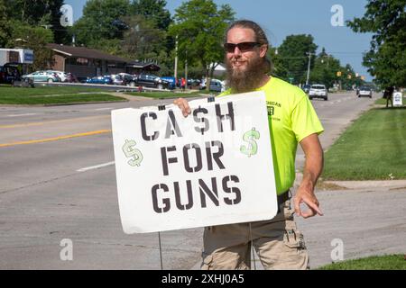 Southfield, Michigan, États-Unis. 13 juillet 2024. Un homme avec un panneau «cash for Guns» a essayé d'éloigner les gens d'un événement de rachat d'armes à feu à l'église épiscopale de David. Il a essayé de les diriger vers un associé tenant une arme automatique de l'autre côté de la rue qui a dit qu'il était collectionneur, mais qui a refusé de dire s'il revendrait les armes qu'il avait achetées. L'église détruisait les armes qu'elle acceptait. Crédit : Jim West/Alamy Live News Banque D'Images